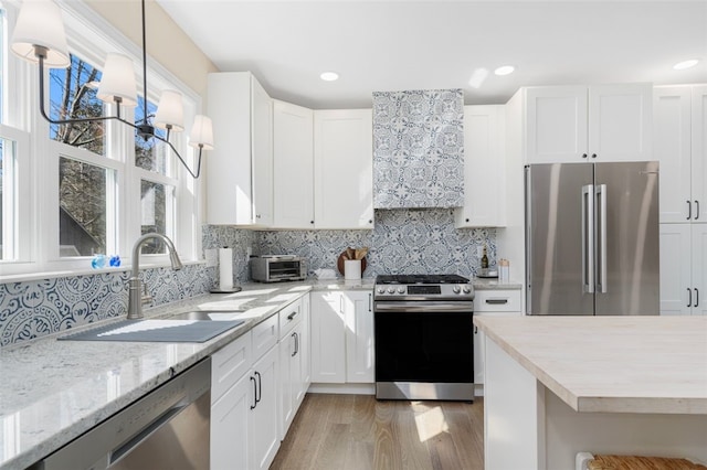 kitchen with stainless steel appliances, white cabinets, a sink, and decorative backsplash