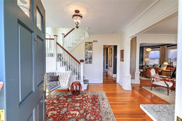 foyer featuring baseboards, stairway, light wood-type flooring, ornate columns, and crown molding