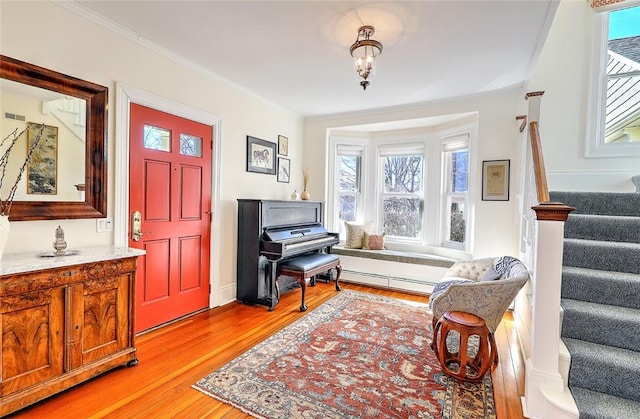 foyer with light wood-type flooring, stairs, baseboard heating, and crown molding