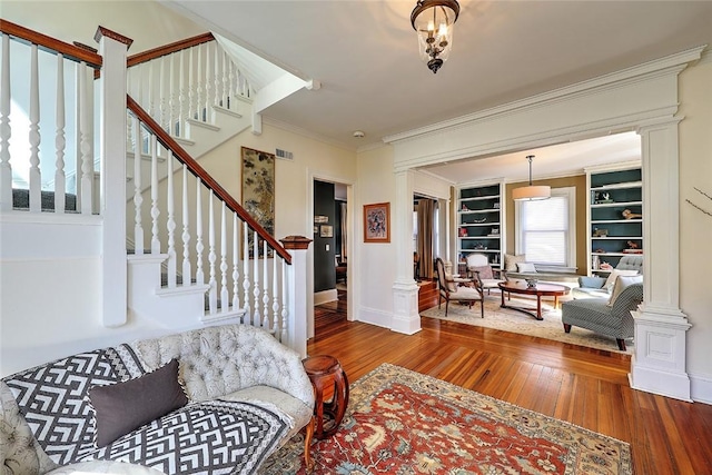 living room featuring hardwood / wood-style flooring, crown molding, visible vents, ornate columns, and stairs