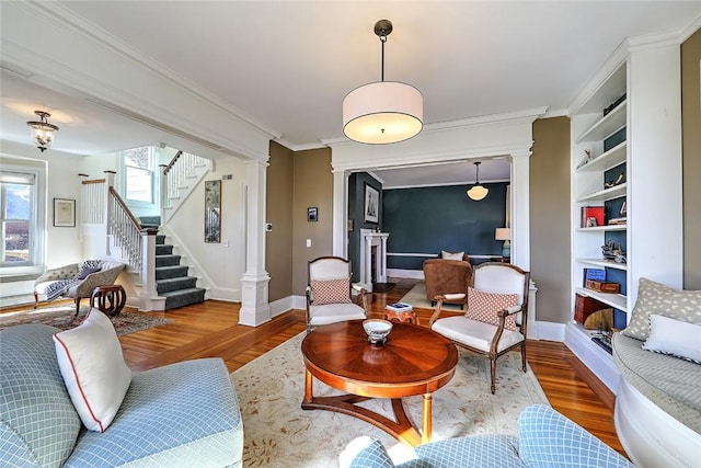 living room with decorative columns, baseboards, stairway, ornamental molding, and wood finished floors