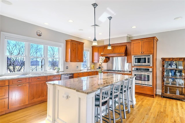 kitchen featuring light stone counters, stainless steel appliances, custom range hood, a sink, and a kitchen island