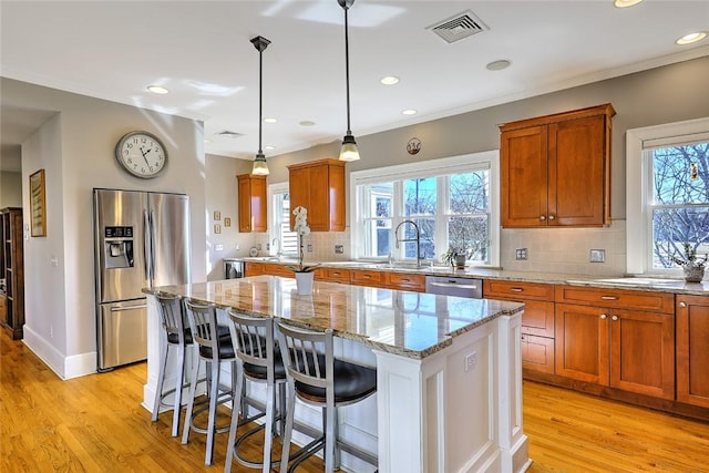 kitchen featuring a center island, stainless steel appliances, visible vents, light wood-style flooring, and light stone countertops