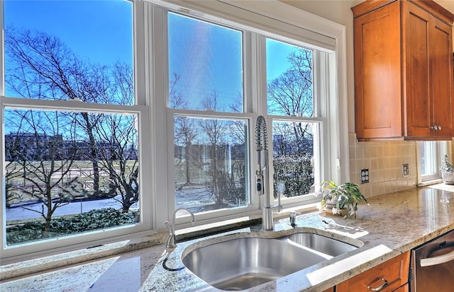 kitchen featuring light stone counters, brown cabinets, a sink, and stainless steel dishwasher