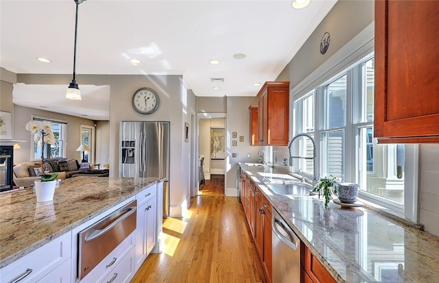 kitchen featuring light wood-style flooring, light stone counters, stainless steel appliances, a sink, and a warming drawer