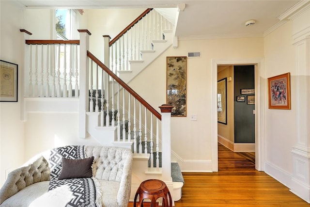 stairs with baseboards, wood finished floors, visible vents, and crown molding