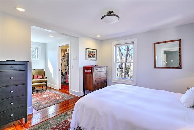 bedroom featuring a walk in closet, dark wood-style flooring, multiple windows, and baseboards