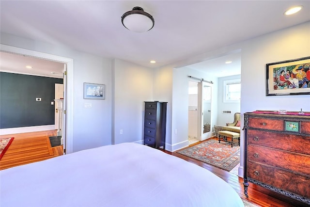 bedroom featuring baseboards, a barn door, wood finished floors, and recessed lighting