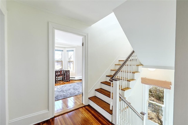 staircase with a baseboard heating unit, a wealth of natural light, and hardwood / wood-style flooring