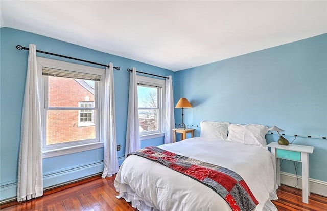 bedroom with a baseboard heating unit, wood finished floors, and baseboards