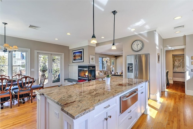 kitchen featuring light stone counters, a warming drawer, light wood finished floors, a glass covered fireplace, and white cabinets