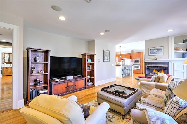 living area with light wood-type flooring, recessed lighting, baseboards, and a glass covered fireplace