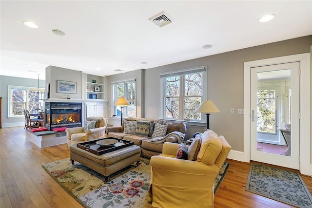 living area with baseboards, visible vents, a glass covered fireplace, wood finished floors, and built in shelves