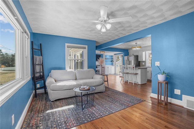 living room featuring baseboards, visible vents, ceiling fan, and wood finished floors