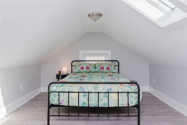 bedroom featuring vaulted ceiling with skylight, baseboards, and wood finished floors