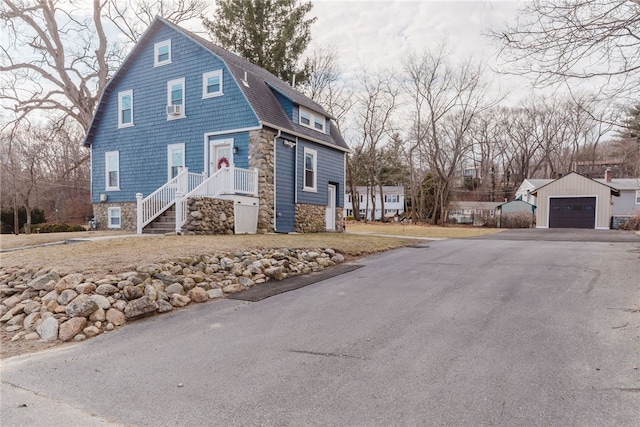 view of front of home with aphalt driveway, roof with shingles, a detached garage, a gambrel roof, and cooling unit