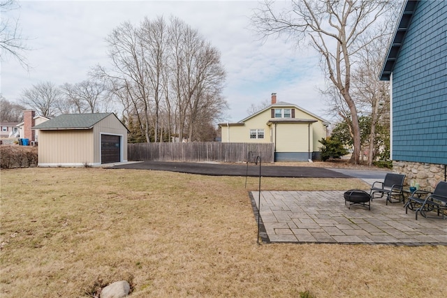 view of yard with an outbuilding, a patio, a fire pit, a garage, and fence