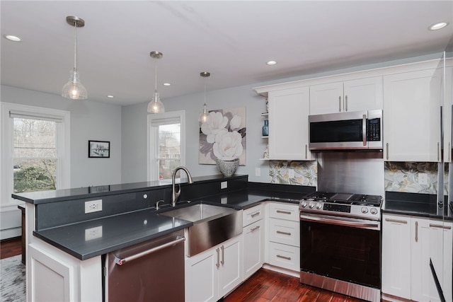 kitchen featuring a peninsula, a sink, appliances with stainless steel finishes, dark countertops, and plenty of natural light