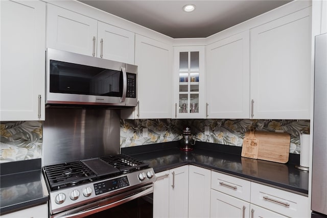 kitchen with tasteful backsplash, dark countertops, glass insert cabinets, stainless steel appliances, and white cabinetry