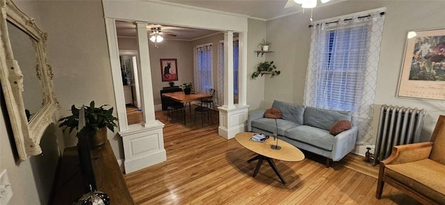 sitting room featuring a ceiling fan, radiator, light wood-style flooring, and ornate columns