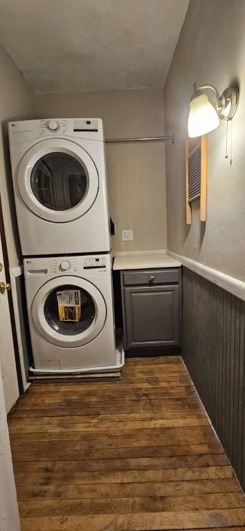 laundry room featuring dark wood-type flooring, stacked washer / dryer, a wainscoted wall, and cabinet space