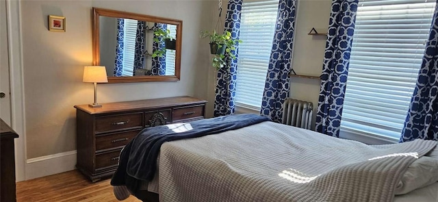 bedroom featuring baseboards, light wood-style flooring, and radiator