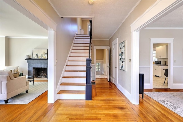 stairs with baseboards, wood-type flooring, ornamental molding, a textured ceiling, and a brick fireplace