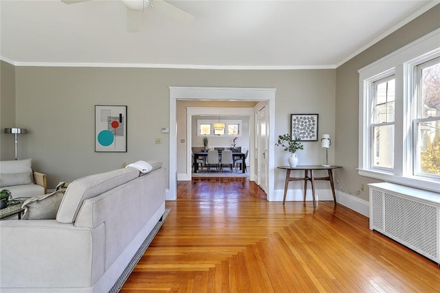 living area featuring parquet floors, radiator heating unit, ornamental molding, ceiling fan, and baseboards