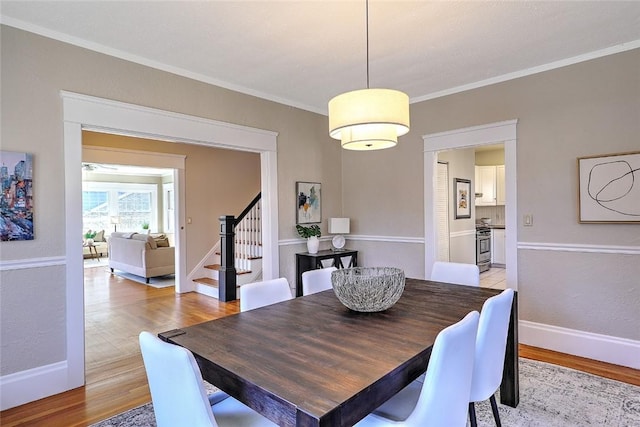 dining area with light wood-type flooring, crown molding, and stairs