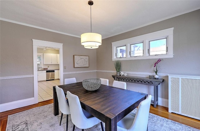 dining space featuring light wood-style floors, ornamental molding, and radiator heating unit