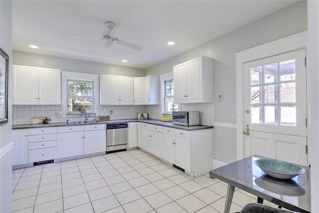 kitchen with light tile patterned floors, a sink, stainless steel dishwasher, tasteful backsplash, and dark countertops