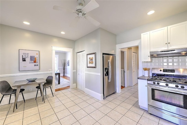 kitchen featuring stainless steel appliances, tasteful backsplash, white cabinets, light tile patterned flooring, and under cabinet range hood