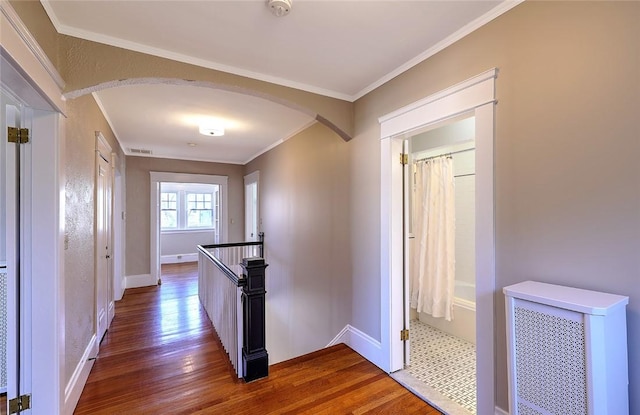 hallway with visible vents, arched walkways, baseboards, dark wood-style floors, and crown molding