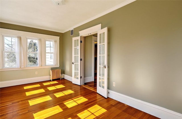 spare room featuring french doors, radiator heating unit, wood finished floors, and baseboards