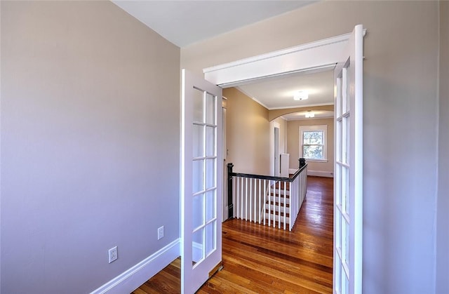 corridor with arched walkways, wood finished floors, an upstairs landing, and baseboards