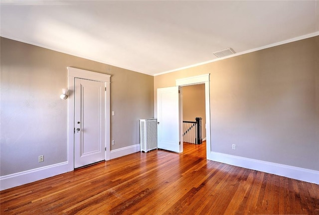 unfurnished room featuring crown molding, wood-type flooring, visible vents, and baseboards