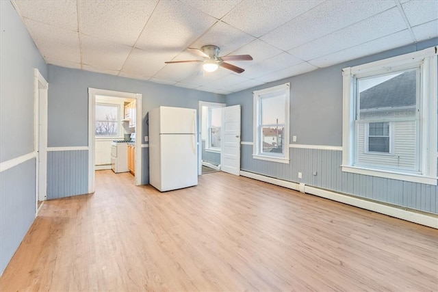 unfurnished room featuring baseboard heating, light wood-style floors, a baseboard heating unit, wainscoting, and a drop ceiling