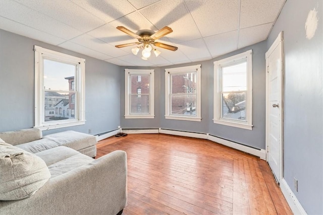 sitting room featuring a paneled ceiling, wood-type flooring, baseboard heating, ceiling fan, and baseboards