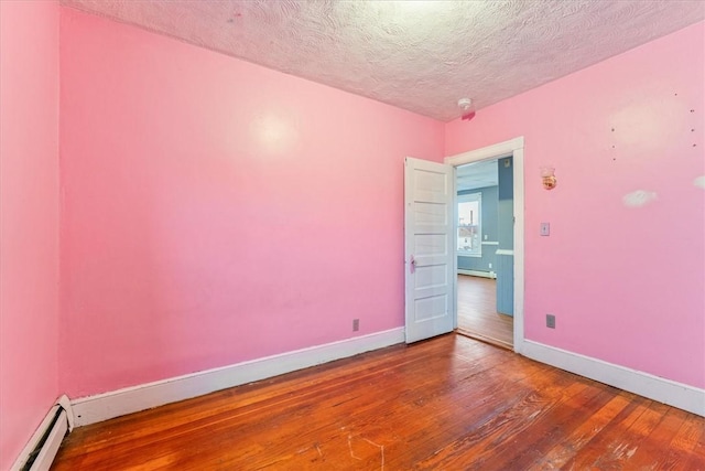 spare room with a textured ceiling, baseboard heating, wood-type flooring, and baseboards