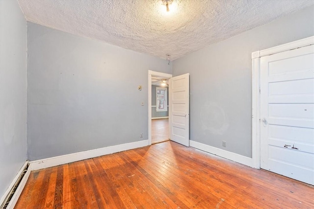 empty room featuring a textured ceiling, a baseboard radiator, hardwood / wood-style flooring, and baseboards