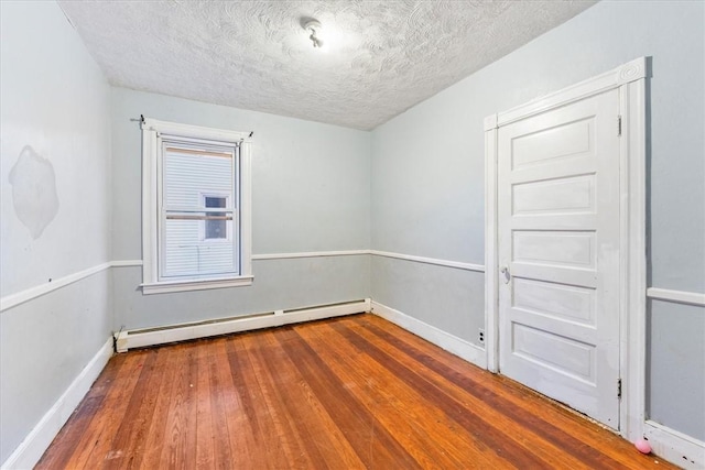 spare room featuring a baseboard heating unit, a textured ceiling, baseboards, and wood finished floors