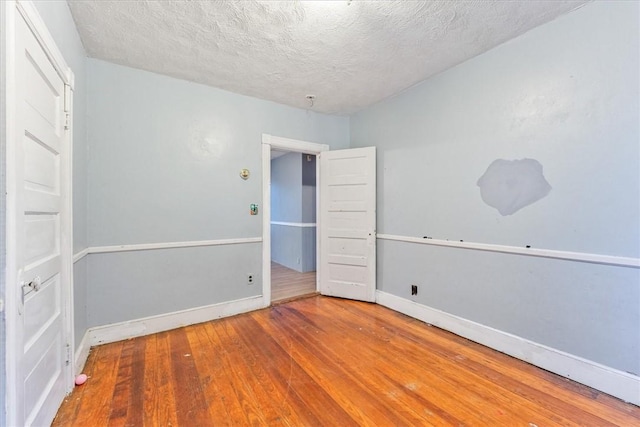 empty room with baseboards, a textured ceiling, and hardwood / wood-style floors