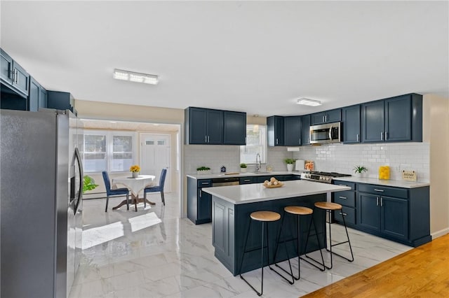 kitchen featuring marble finish floor, stainless steel appliances, light countertops, decorative backsplash, and a kitchen bar