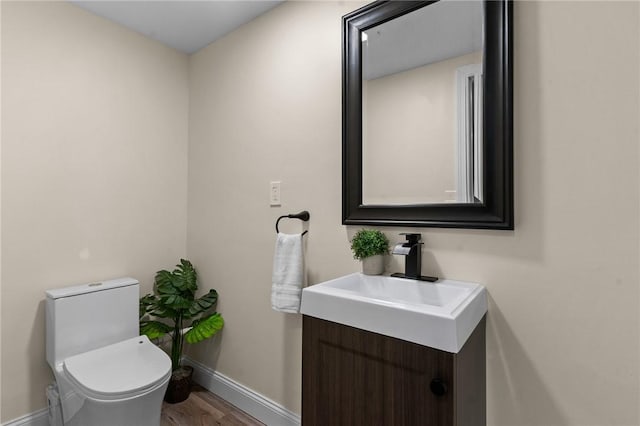 half bath with toilet, baseboards, wood finished floors, and vanity