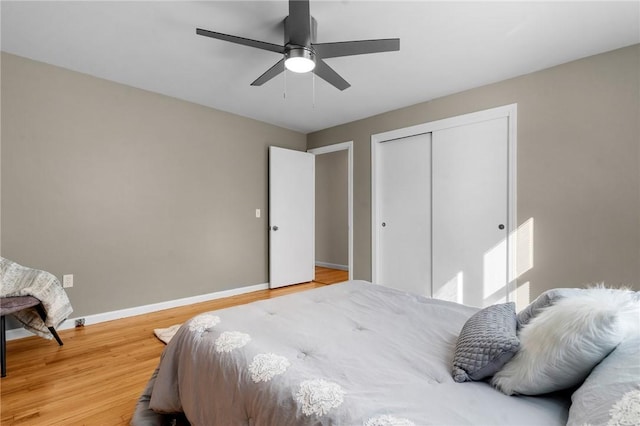 bedroom with light wood finished floors, a ceiling fan, baseboards, and a closet