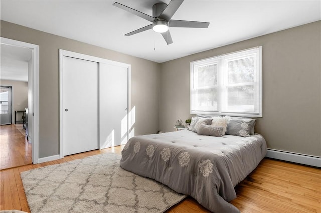 bedroom with a baseboard radiator, hardwood / wood-style flooring, a ceiling fan, baseboards, and a closet