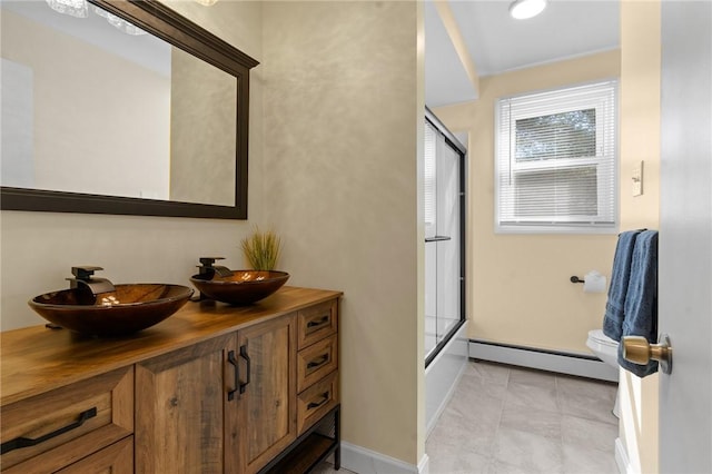 full bathroom with double vanity, baseboard heating, a sink, and toilet