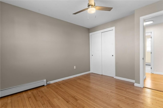 unfurnished bedroom featuring a baseboard heating unit, a ceiling fan, baseboards, light wood-style floors, and a closet