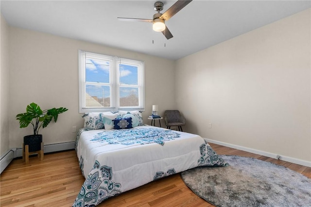 bedroom with a baseboard heating unit, light wood-type flooring, and baseboards