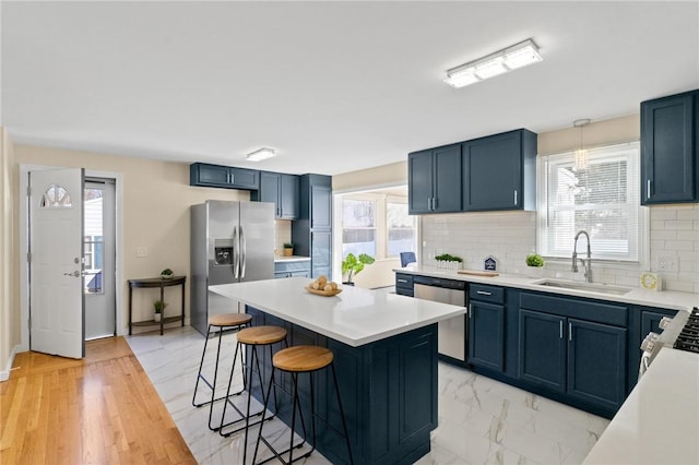 kitchen featuring marble finish floor, stainless steel appliances, light countertops, a kitchen bar, and a sink